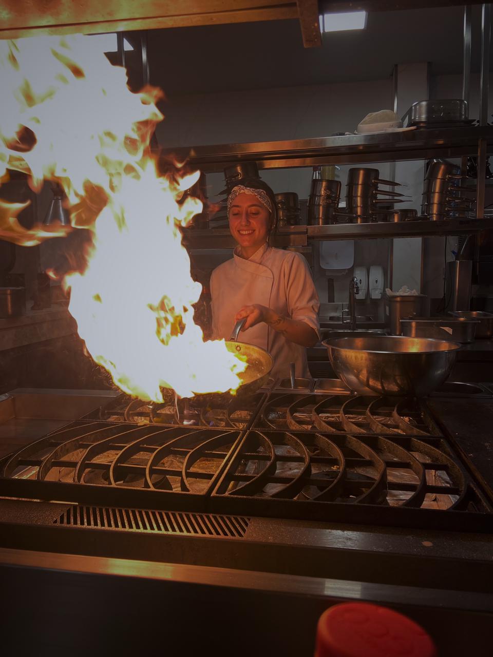 Julia Di Loreto flambando um prato na cozinha.